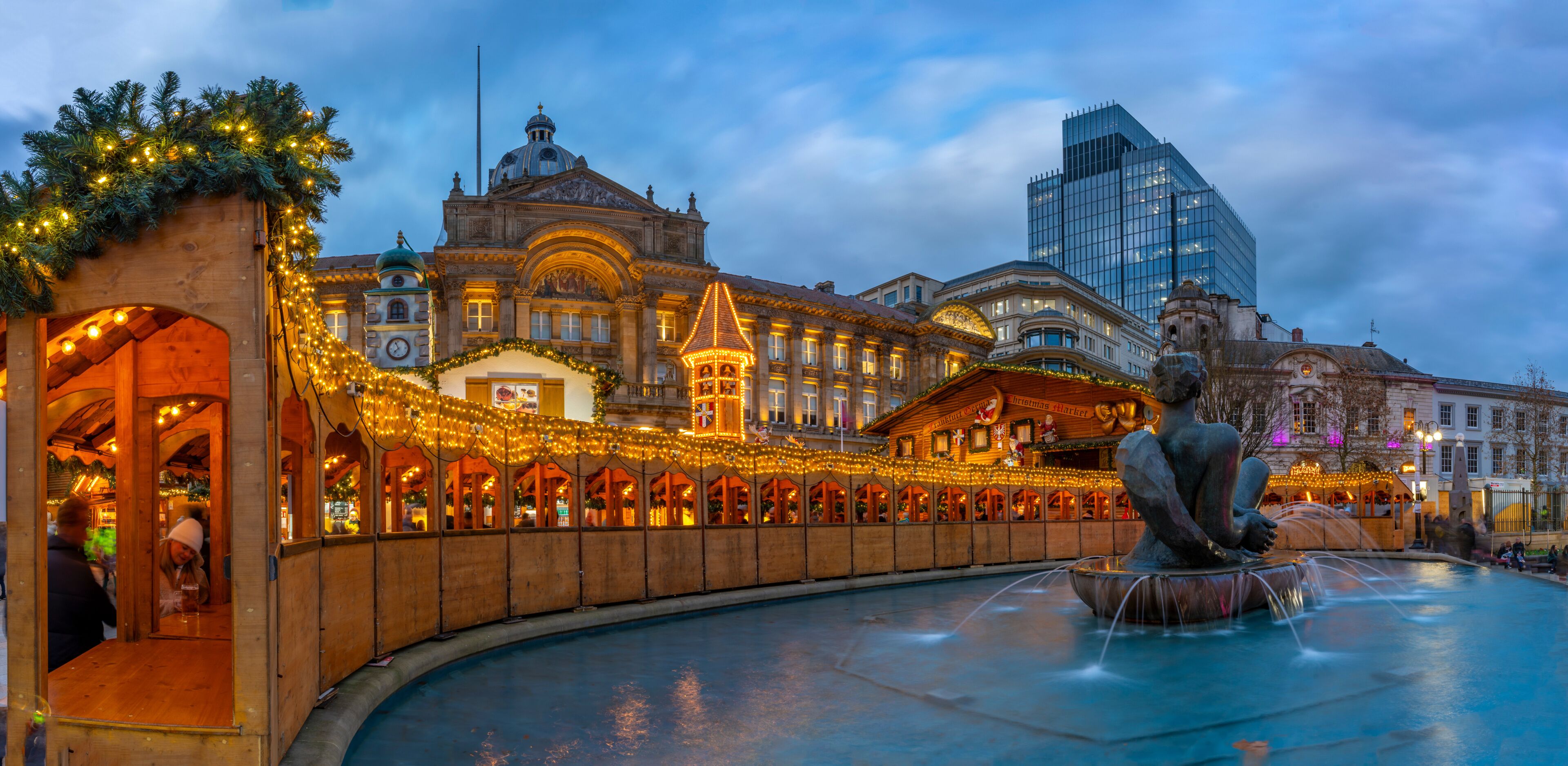 A historic building with ornate architecture, a fountain with a statue, and festive lights.