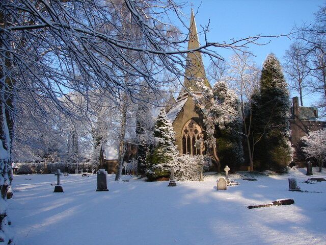 A snow-covered church with a tall spire, surrounded by snow-laden trees and gravestones.