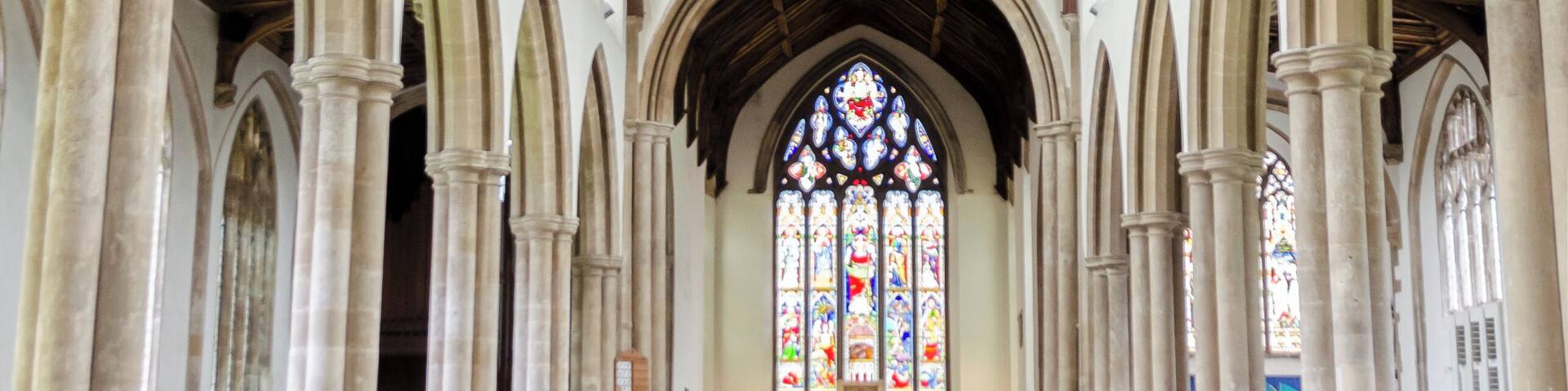 A church interior with wooden pews, arched ceilings, and stained glass windows.