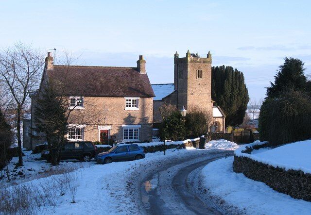 View along Low Field Lane, Cold Kirby, North Yorkshire, looking southeast to the Old School House (left) and the west tower of St Michael's parish church, in snow