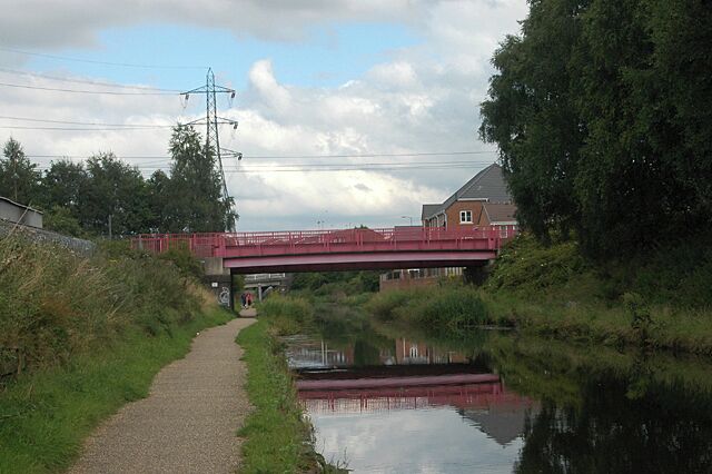 Un puente rojo sobre un canal, con una casa y árboles al fondo.