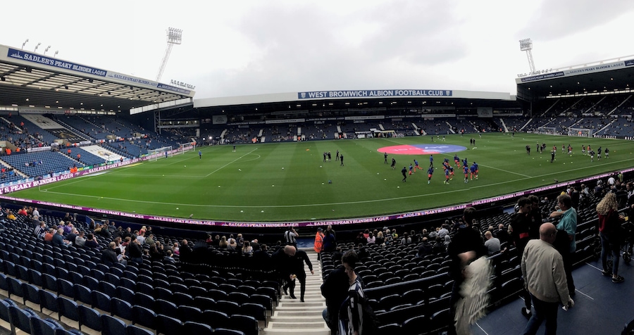 A football stadium with a large field, seating areas, and a partially filled crowd.