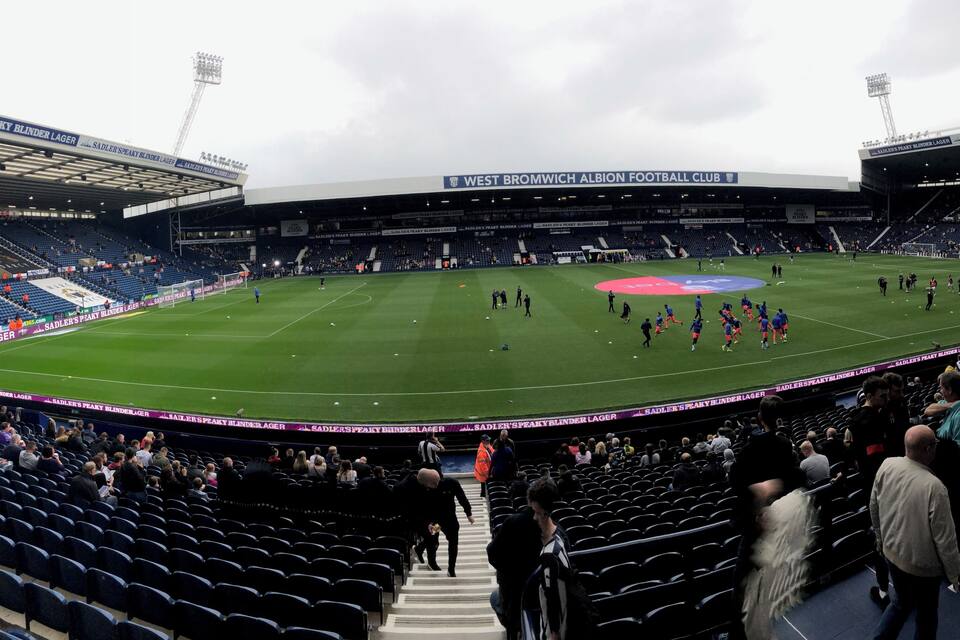 A football stadium with a large field, seating areas, and a partially filled crowd.