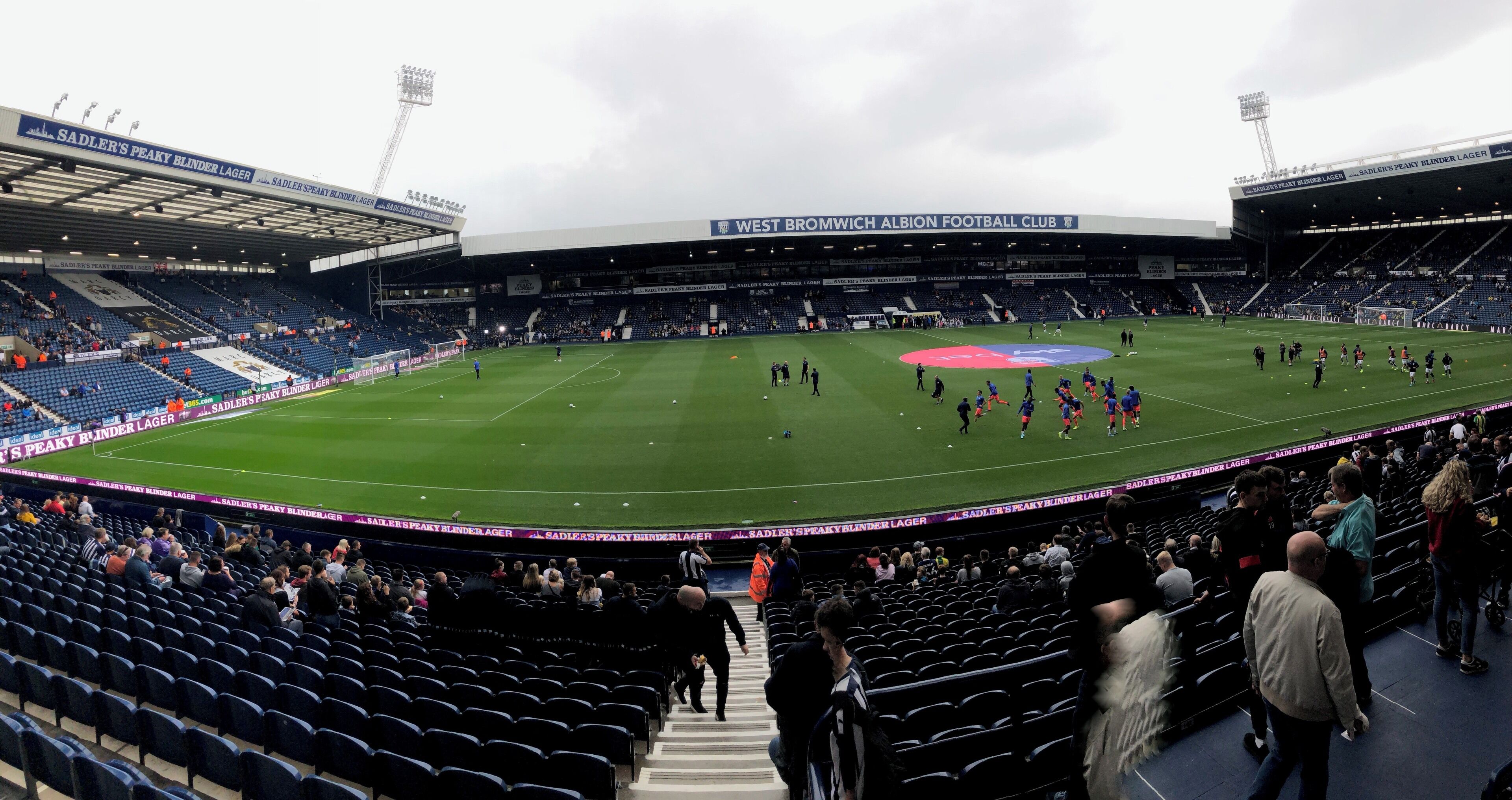 A football stadium with a large field, seating areas, and a partially filled crowd.