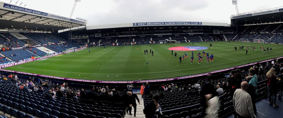 A football stadium with a large field, seating areas, and a partially filled crowd.
