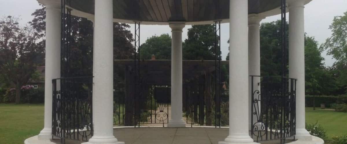 A white gazebo with a dome roof and columns, surrounded by gravel and greenery.
