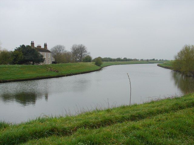A narrow waterway flanked by grassy banks and a house.