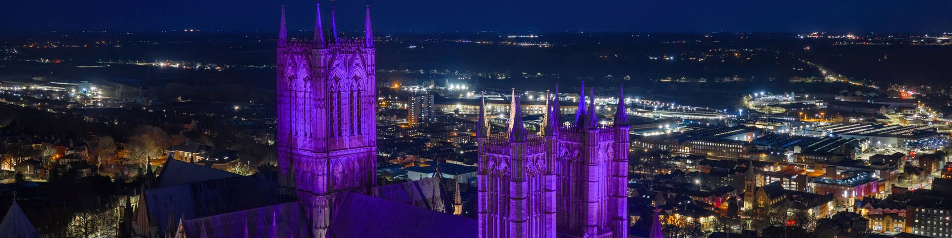 A Gothic cathedral with twin spires and a large central tower, surrounded by a cityscape at night.