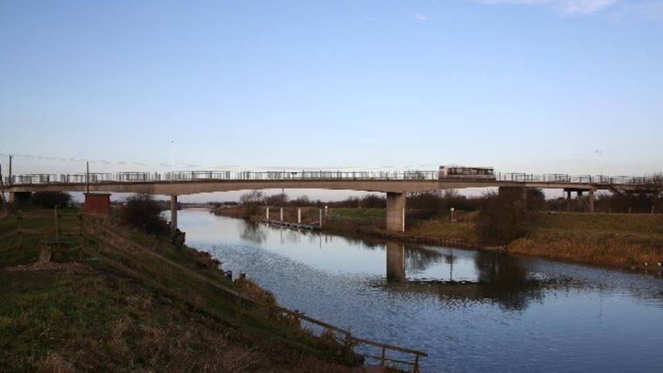 A bridge over a calm river with grassy banks and a clear sky.