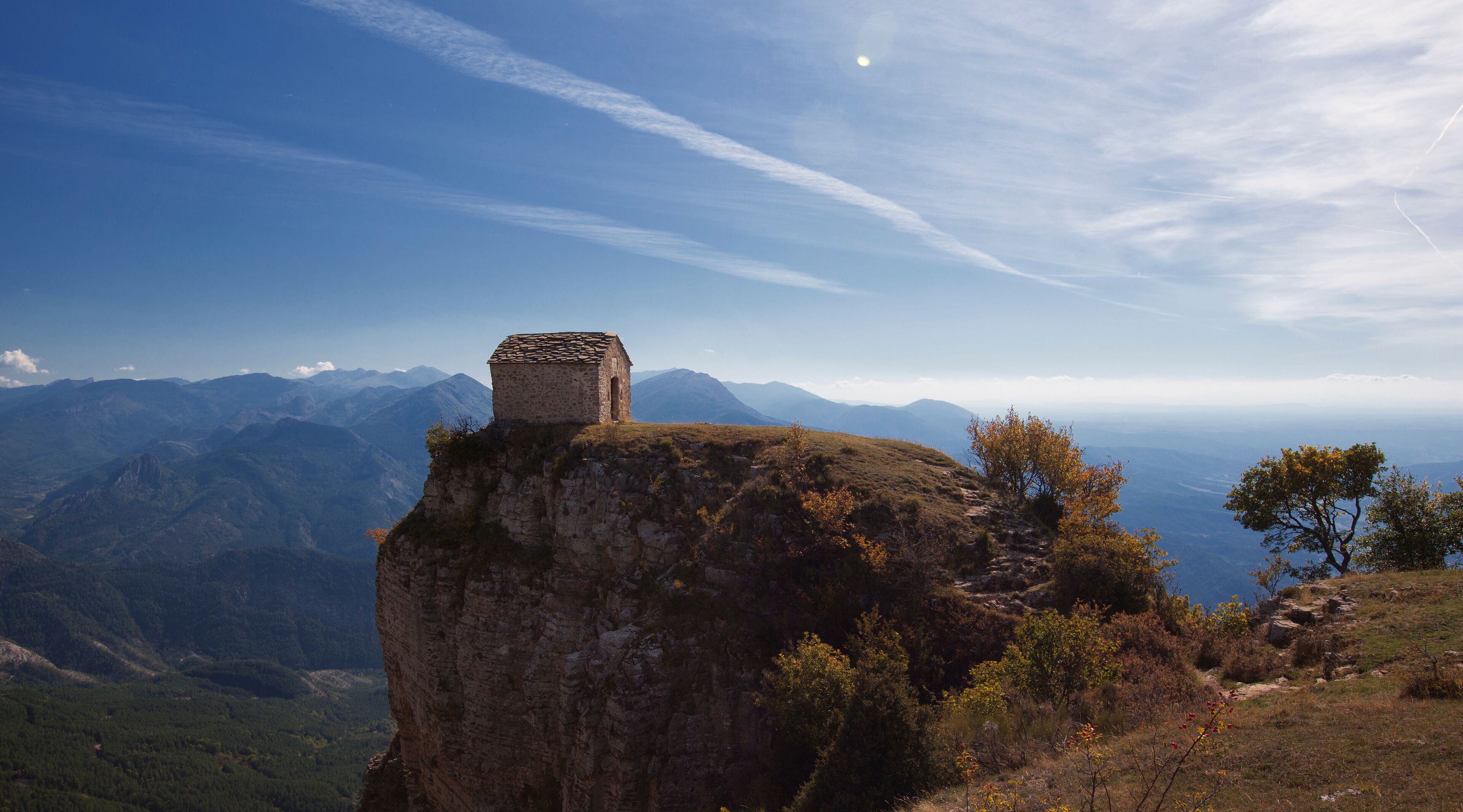 A stone structure on a cliff overlooking a mountainous landscape.