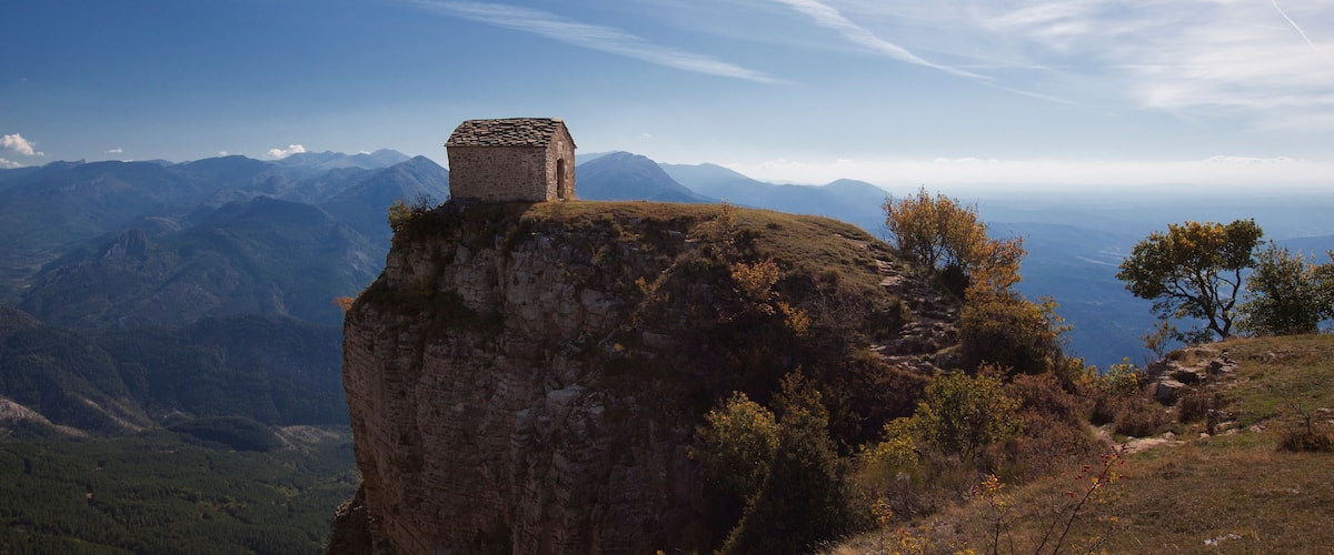 A stone structure on a cliff overlooking a mountainous landscape.