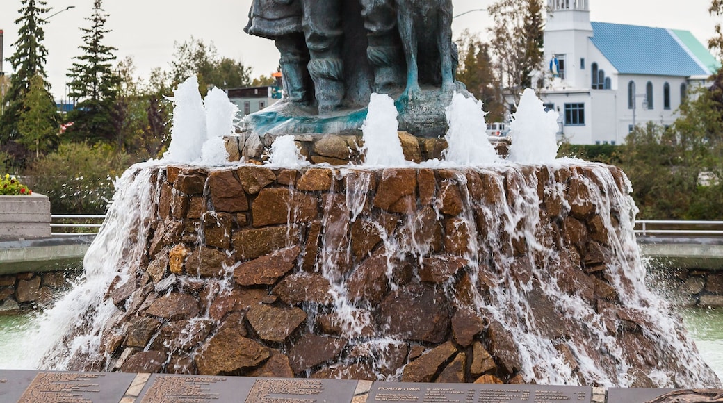 A statue with a child, a church with a blue roof, and a stone fountain.