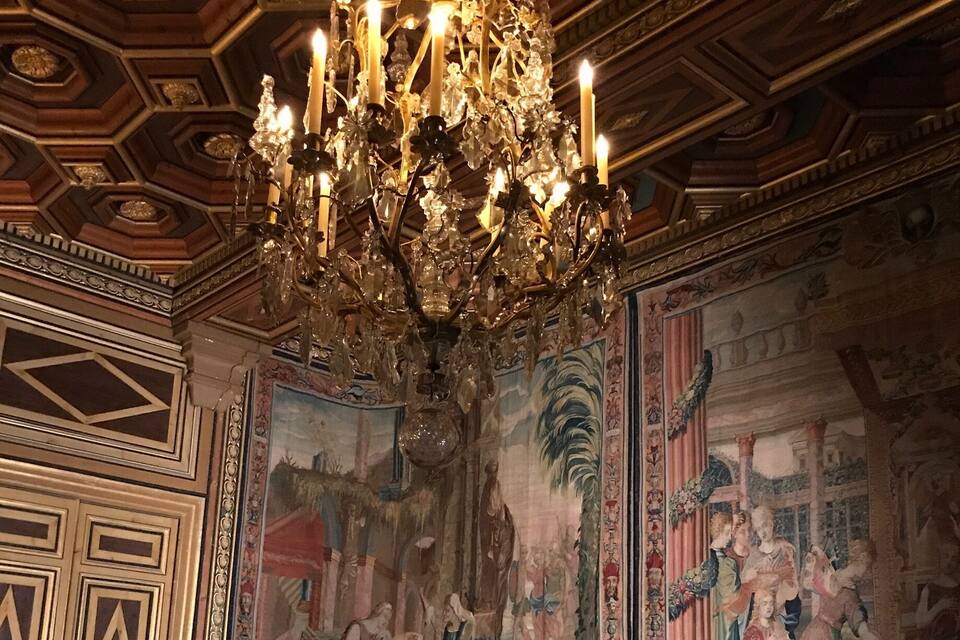 An ornate room with a large chandelier, a mural, and a sofa with floral upholstery.