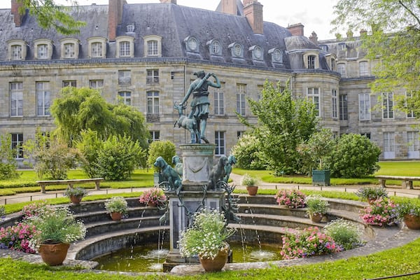 Un bâtiment historique doté d’une fontaine et de statues, situé dans un jardin bien entretenu.