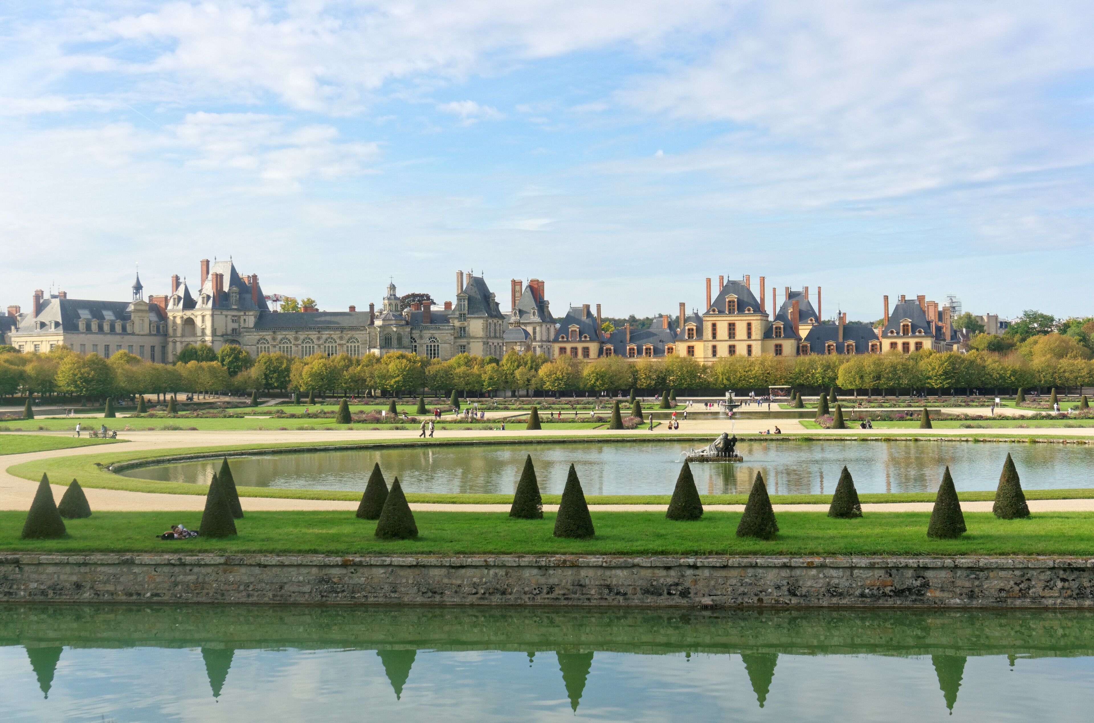 A historic building complex with a large pond and neatly trimmed trees.