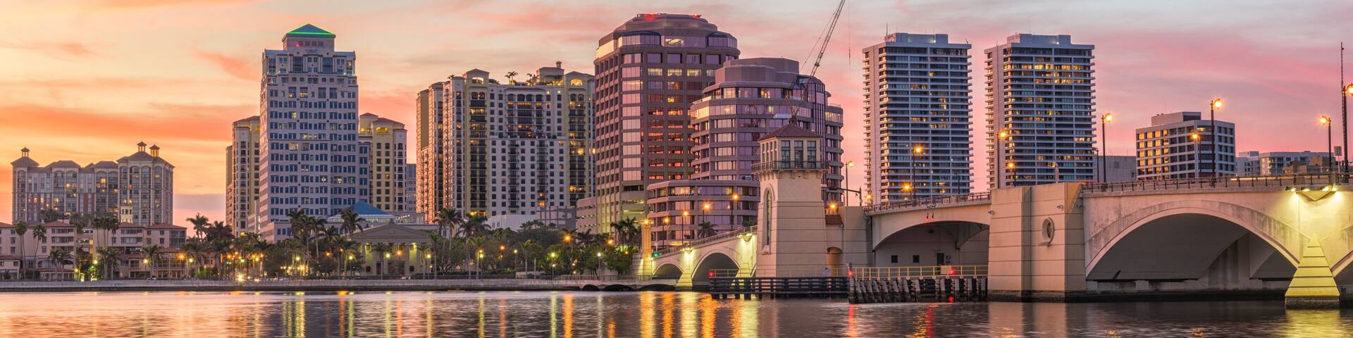 A city skyline at sunset with a bridge reflecting the buildings and lights.