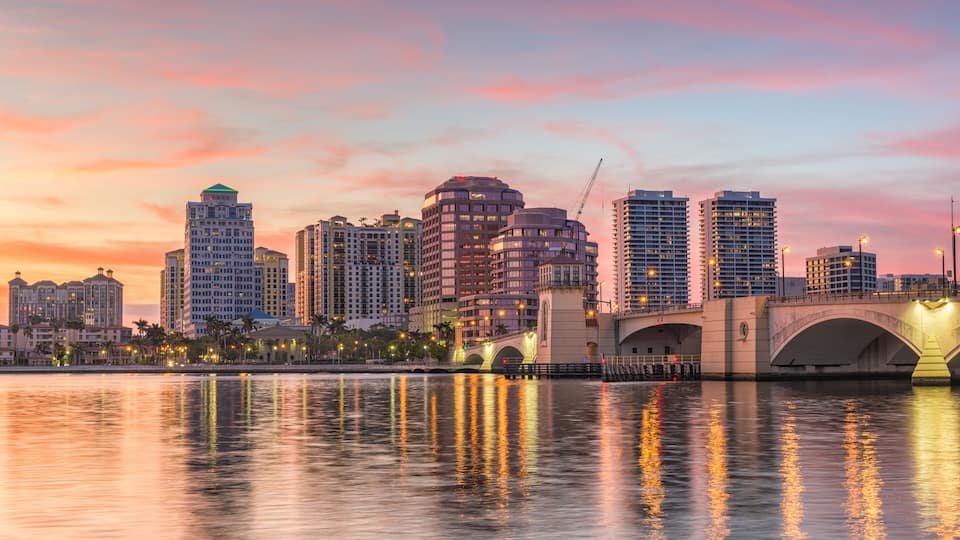 A city skyline at sunset with a bridge reflecting the buildings and lights.