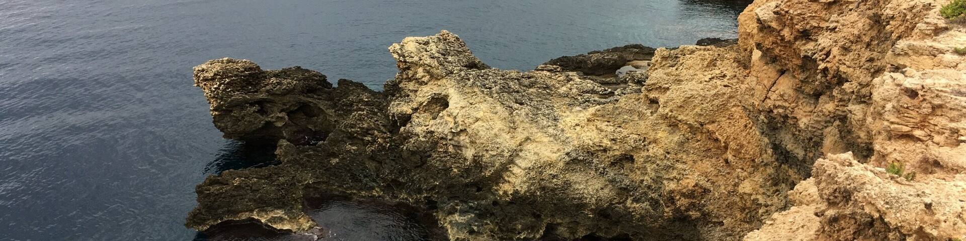 A coastal cliff with clear blue water and rocky formations.