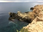 A coastal cliff with clear blue water and rocky formations.