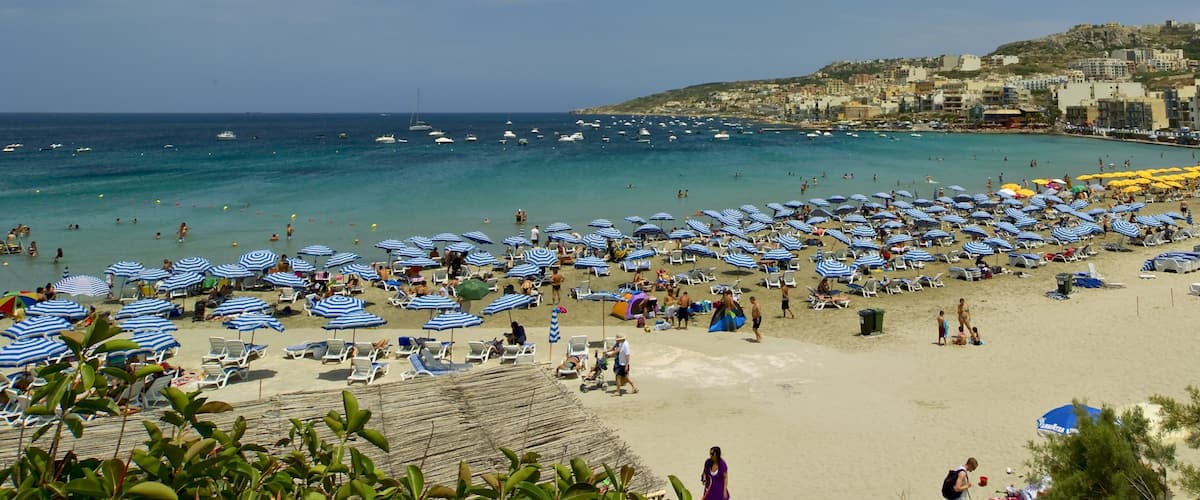 A crowded beach with numerous blue and white striped umbrellas and sun loungers.