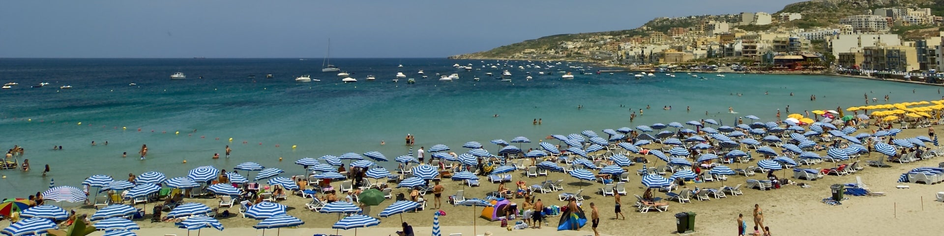 A crowded beach with numerous blue and white striped umbrellas and sun loungers.