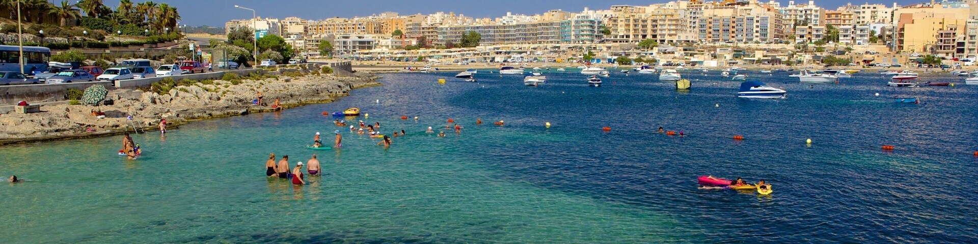 Un pueblo costero con aguas cristalinas, barcos y gente nadando.