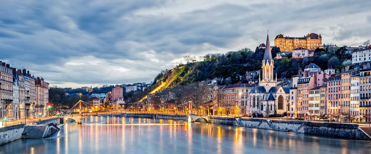 A river with a bridge, historic buildings, and a castle on a hill.