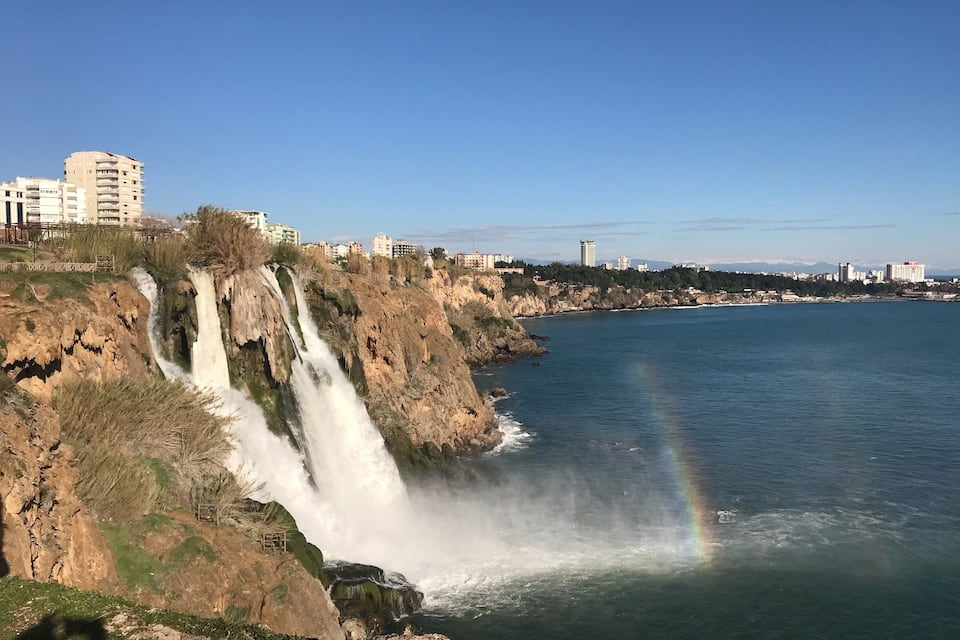 Une cascade se jetant dans un plan d’eau, avec un arc-en-ciel visible au loin.