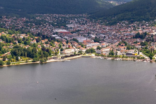 Une vue panoramique d’une ville située au bord d’un lac, avec des quartiers résidentiels, une place centrale et des collines environnantes.