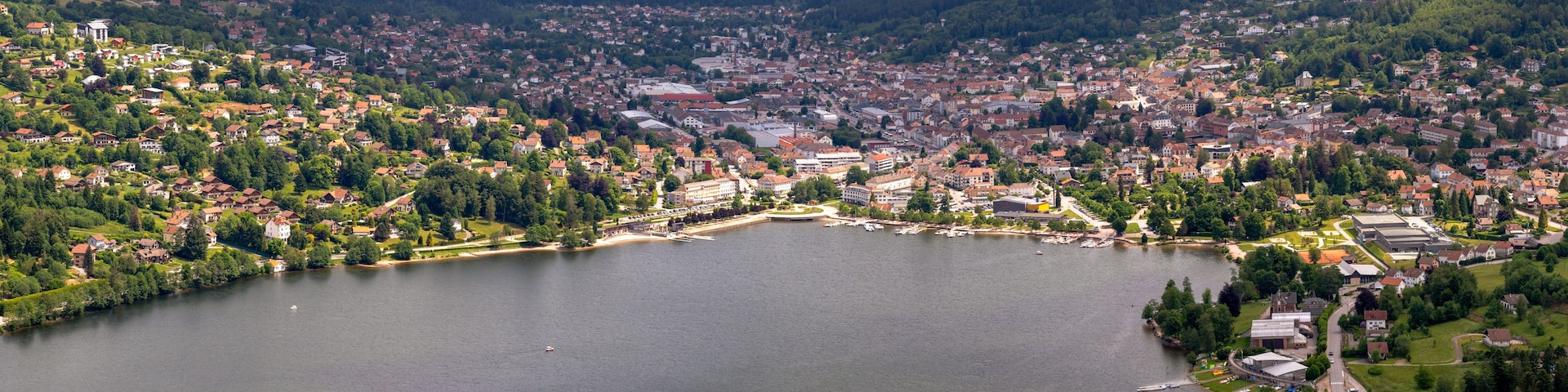 Une vue panoramique d’une ville située au bord d’un lac, avec des quartiers résidentiels, une place centrale et des collines environnantes.