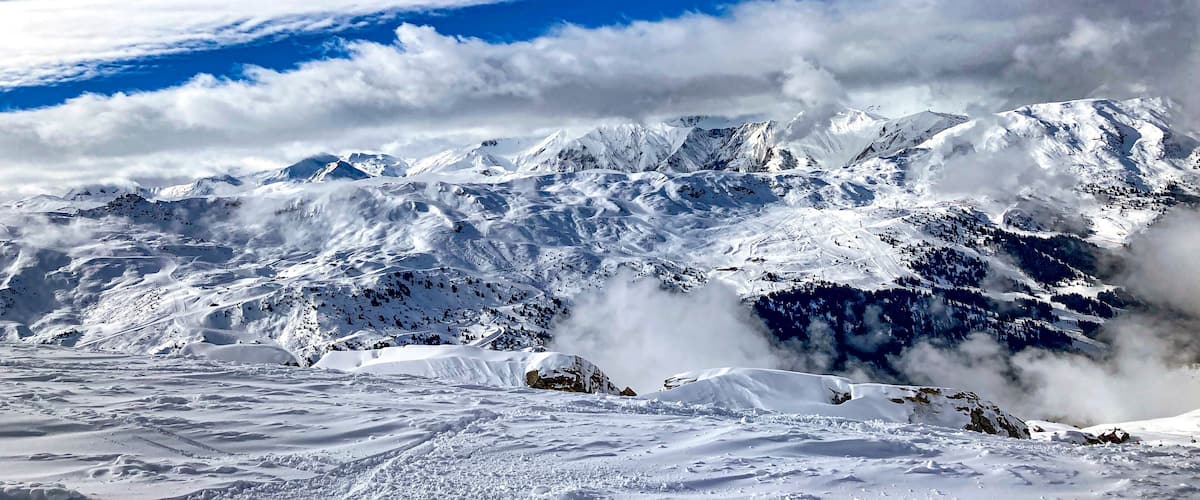 A snow-covered mountain range with a clear blue sky and clouds.