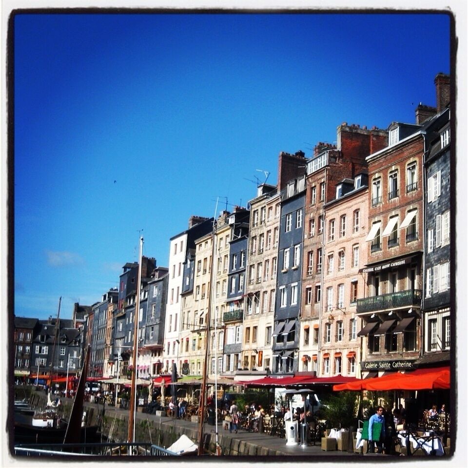 A row of colorful buildings along a waterfront with outdoor cafes and people walking.