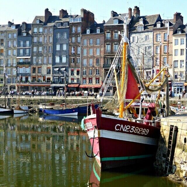 Ein rotes Fischerboot mit der Nummer CN238289 liegt in einem Hafen vor Gebäuden.