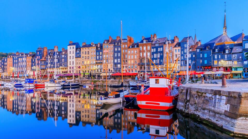 A harbor with boats, a church steeple, and colorful buildings reflecting on the water.