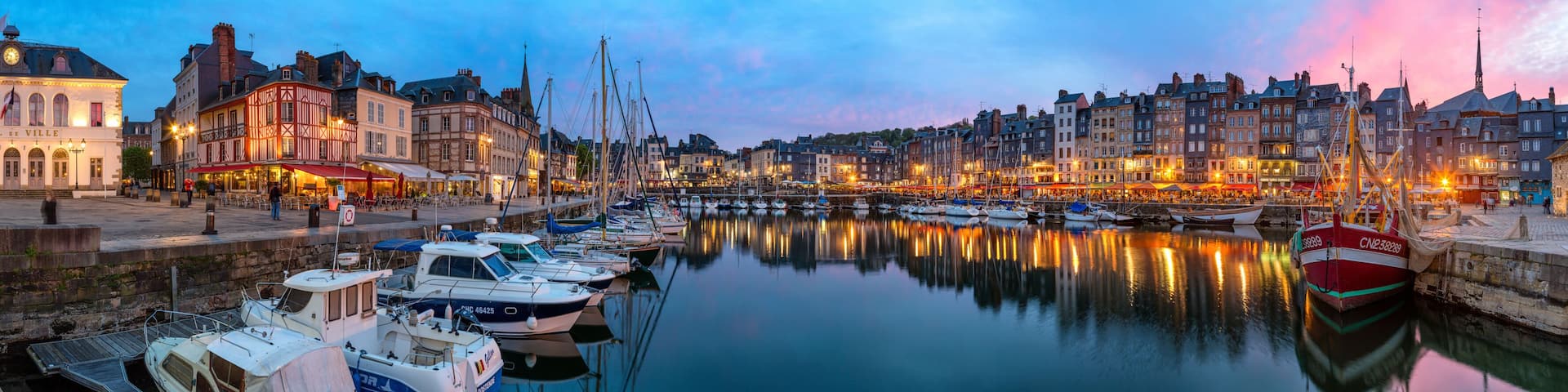 A harbor with boats docked, a hotel named 'HOTEL DE VILLE,' and historic buildings along the waterfront.