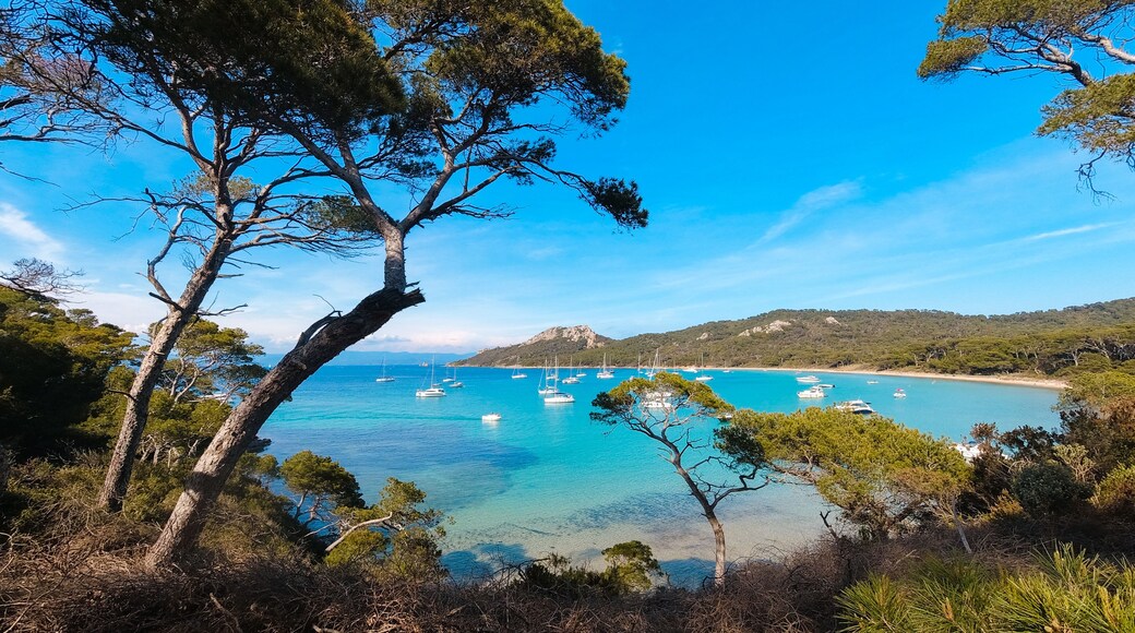 Un paisaje costero con aguas turquesas cristalinas, barcos anclados y colinas al fondo.