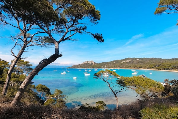 Un paysage côtier avec une eau turquoise cristalline, des bateaux amarrés et, en arrière-plan, des collines.