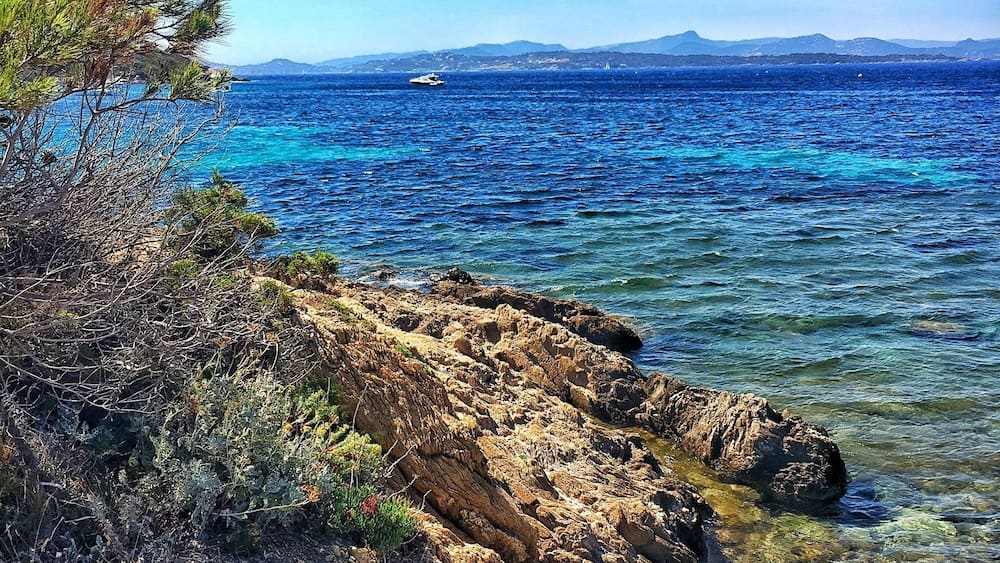 Une côte rocheuse bordée d’eaux d’un bleu limpide et dominée par des montagnes lointaines.