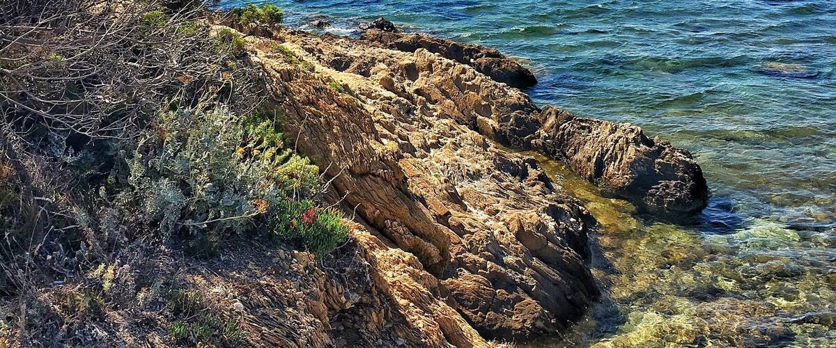 A rocky coastline with clear blue waters and distant mountains.