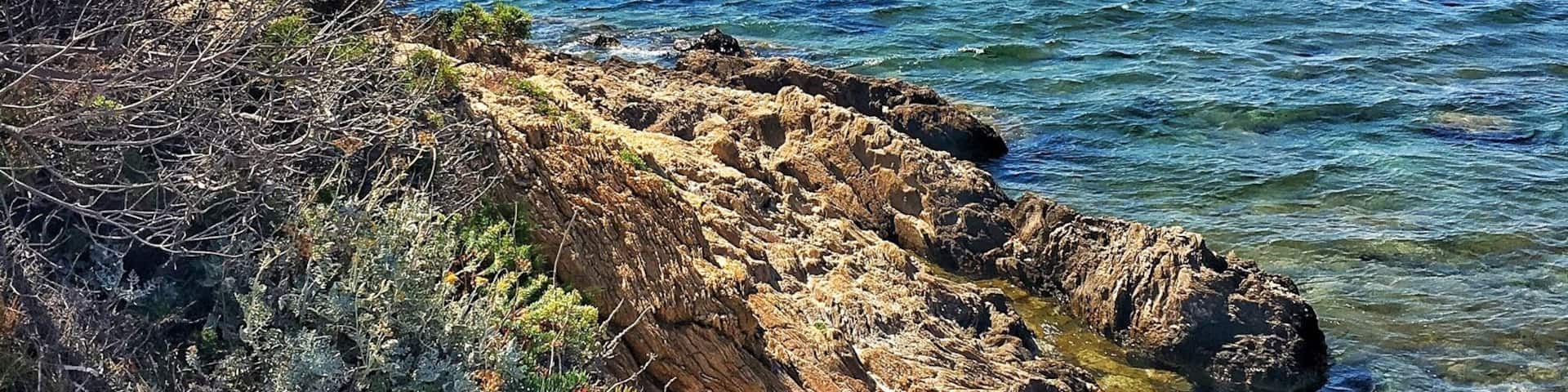A rocky coastline with clear blue waters and distant mountains.