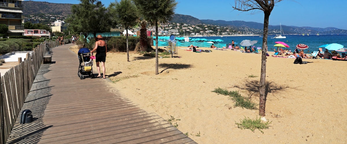 A beach with a wooden boardwalk, beach umbrellas, and a clear blue sky.