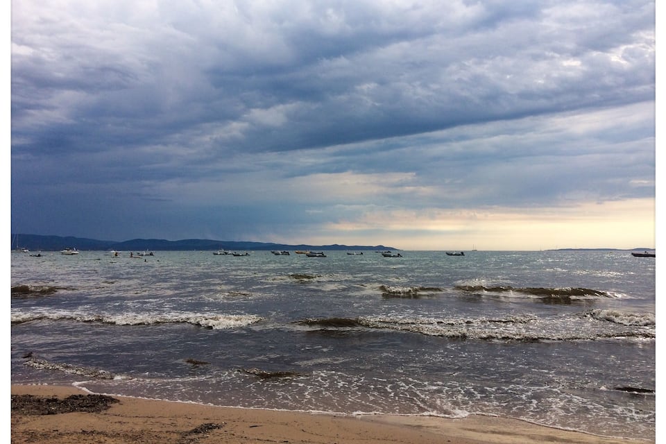 A beach with waves, boats, and a cloudy sky.