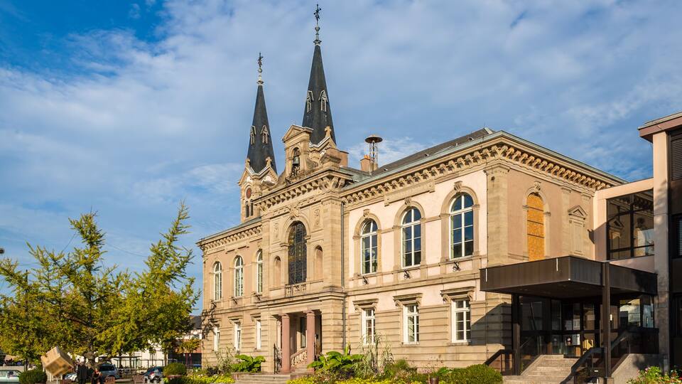 A historic building with two tall spires and a courtyard with a fountain and flowers.