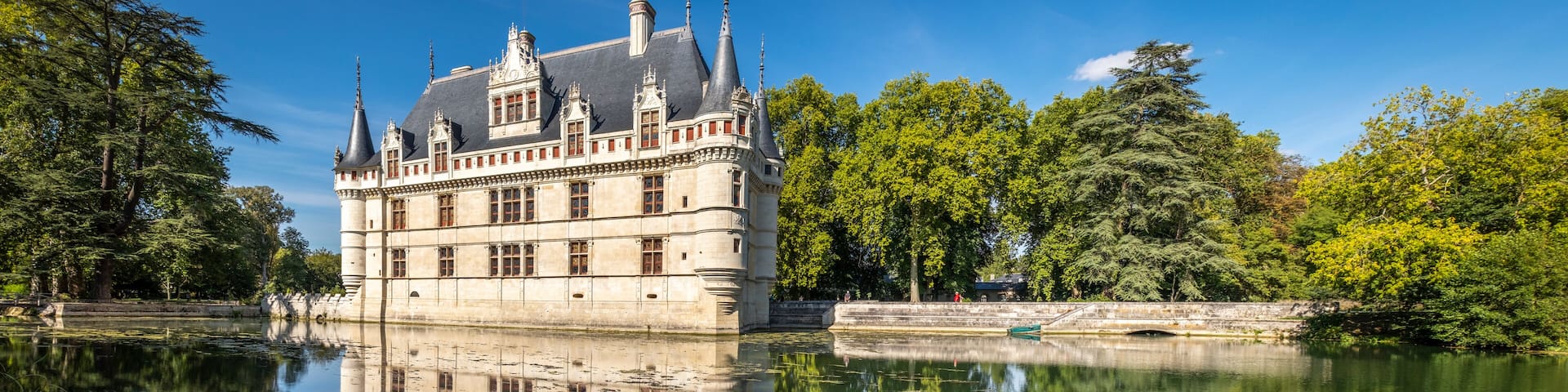 A historic castle with a moat, surrounded by lush greenery and trees.
