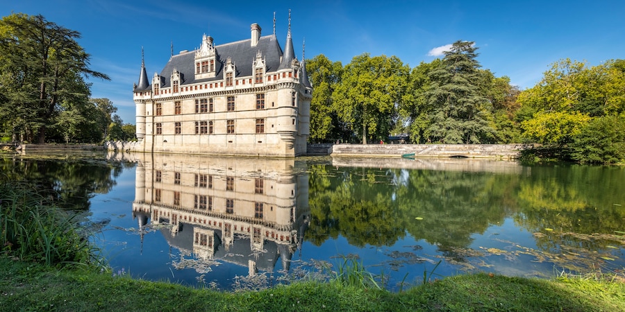 A historic castle with a moat, surrounded by lush greenery and trees.