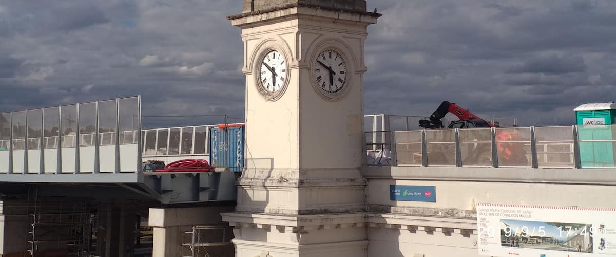 A clock tower with a weather vane on top, surrounded by scaffolding and construction equipment.