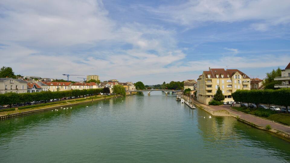 A river with a bridge, buildings, and parked cars.