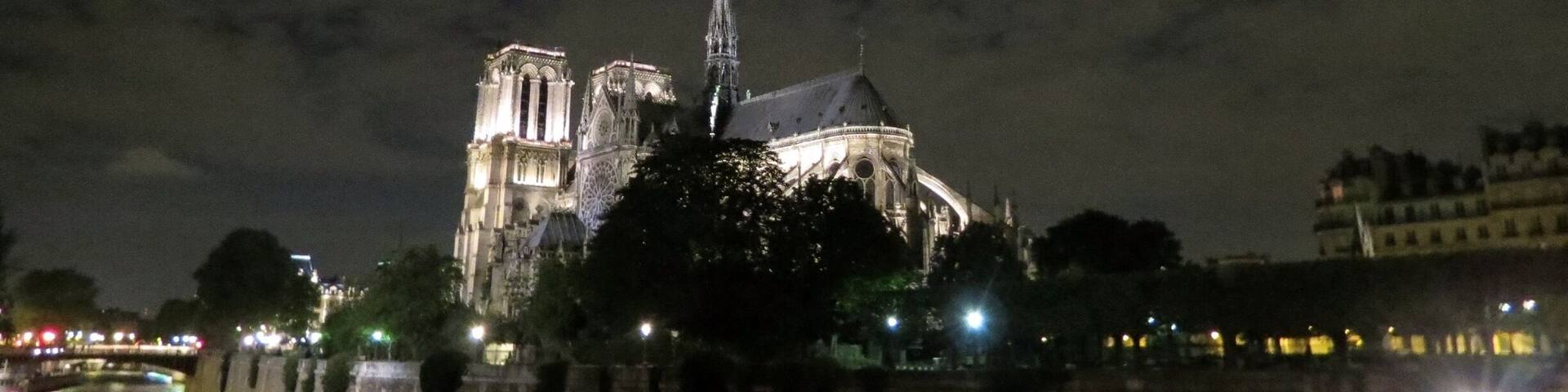 La Catedral de Notre Dame de noche, con agujas iluminadas y un río al frente.