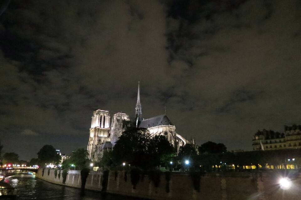 Notre-Dame Cathedral at night with illuminated spires and a river in the foreground.