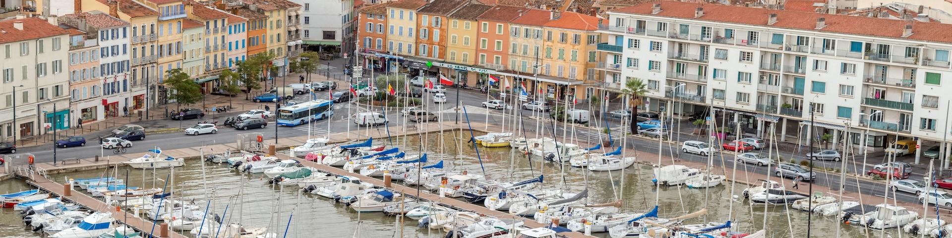 Marina cheia de barcos, cercada por edifícios coloridos e uma rua movimentada.